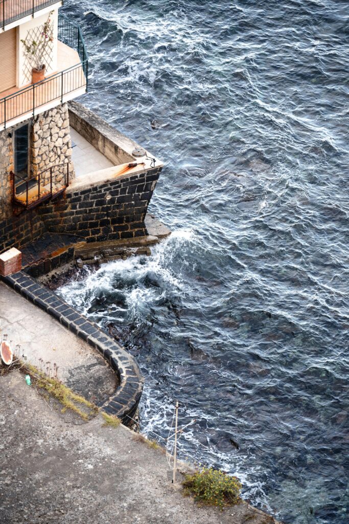 Stone house with balconies by the ocean edge, waves crashing below
